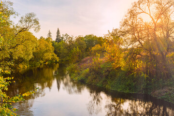 Scenic view of beautiful sunset or sunrise above the pond or river at autumn evening with cloudy sky. Sunbeams pass through the trees. Nature landscape background