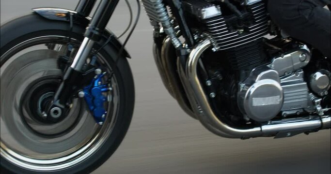 Close-up of a motorcycle riding on a road at high speed. Side view. Driving Bike on Streets. Speed Motion in Cityscape. Fast TRACKING Shot of a biker riding his custom built cafe racer through city.
