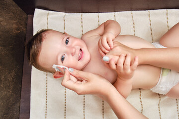 A mother washes the face of a happy toddler baby boy with a cotton pad. Mom cleanses the skin of a...
