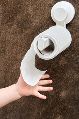 Toddler baby reaches for toilet paper, child s hand with hygiene products close-up. White toilet paper in the home bathroom and a baby hand