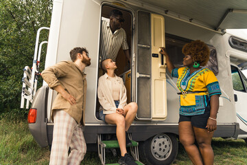 Laid-back group of multi-cultural and multi-ethnic friends standing in front of their camper and...