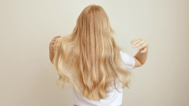 Blonde woman stands with her back throws long wavy hair. The concept of dyeing and hair extensions.