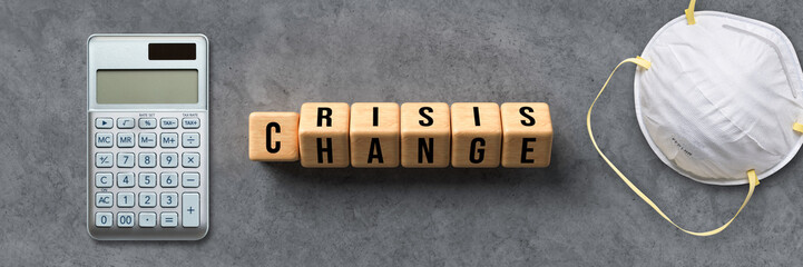 a calculator, a mask and cubes with the words CRISIS and CHANGE on concrete background
