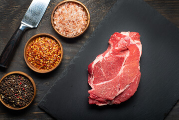 Fresh meat, salt, pepper, and knife on a dark table. View from above.