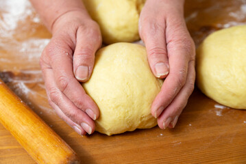 Female hands hold a pizza dough ball. Flour and portions of dough are on the table. Close-up.