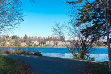 View lakeside coastal trail to row of duplex houses with downtown Anchorage buildings in background...