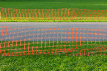 Fototapeta premium Plastic orange barricade net along sidewalk with green grass, Construction safety fence protected from construction site work, Closed area for maintenance or repair under ground of street in the park.