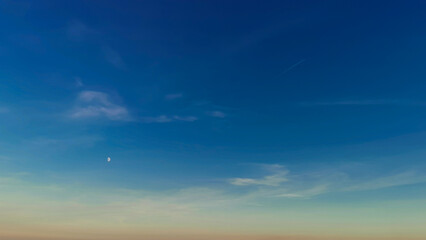 Luna bianca nel cielo azzurro e scia di aereo