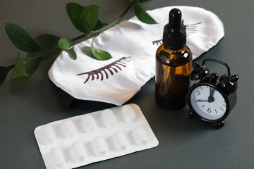 pills, dropper bottle with medicine, silk gray sleep mask and little black alarm clock