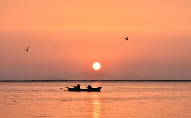 Naklejka na ściany i meble Fishing boat silhouette on a sea at sunset. Seagulls flying on the sea. 