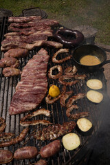 Food. View of the iron grill stacked with roasting meat and offals with a smokey fire. 
