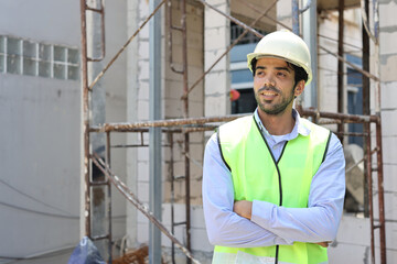 Caucasian technician civil engineer or specialist inspector standing and crossed arms while looking away with happy face after project complete at Industrial building site. Construction concept