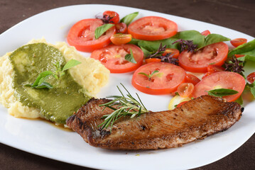 fried tilapia fish filet served on plate with tomato salad and mashed potatoes with herb pesto