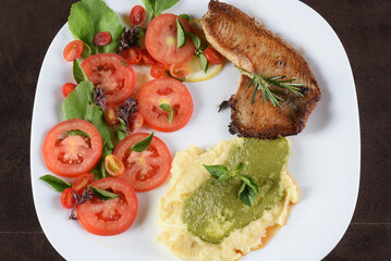 fried tilapia fish filet served on plate with tomato salad and mashed potatoes with herb pesto