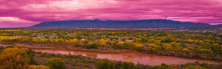 Rio Grand River, autumn landscape with colorful cottonwood trees, and dramatic pink stormy clouds at sunset over Albuquerque city skyline, New Mexico, USA - obrazy, fototapety, plakaty