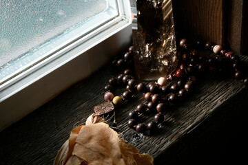 An image of a smoky quartz tower wrapped with meditation beads on a wooden window sill with soft...