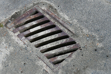 An image of a rectangular shaped storm drain cover on a paved street.