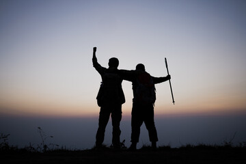 Silhouette of cheering hiking men open arms to the sunrise stand on mountain