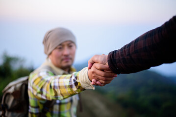 Close-up of Two male hikers helping each other climb up a mountain