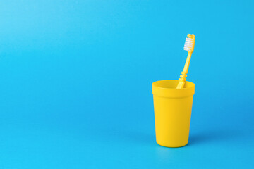 A yellow plastic cup with a yellow toothbrush on a blue background.