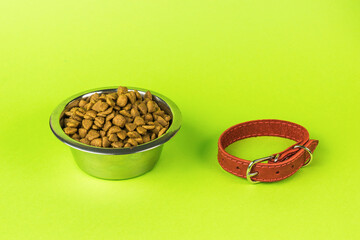 A bowl with dry dog food and a red collar on a green background.