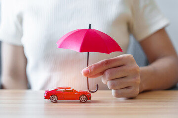 Businesswoman hand holding red umbrella and cover red car toy on table. Car insurance, warranty,...