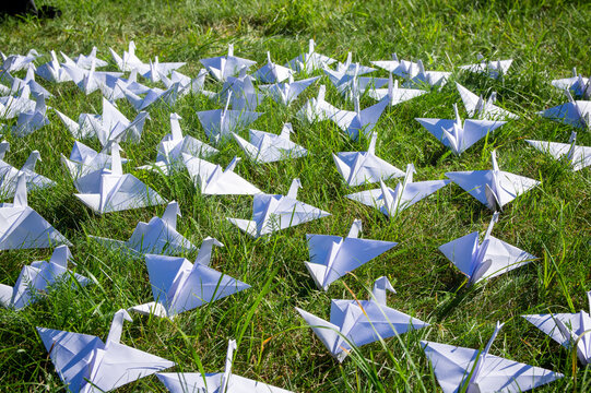 Japanese folded Origami cranes on fresh grass. Hundreds handmade paper birds on green field with copy space. 1000 thousand crane tsuru sculpture topic. Symbol of peace, faith, health, wishes and hope 