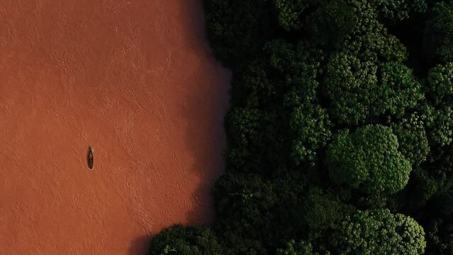 Un bote de color marr&oacute;n en el r&iacute;o remando en la selva con toma a&eacute;reo