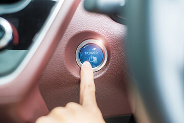 Finger press a car ignition button or START engine inside modern electric automobile. Keyless,...
