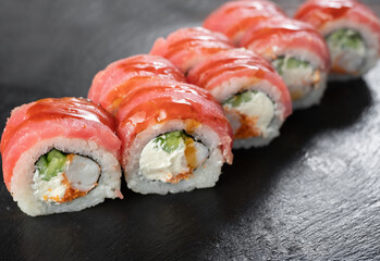 uramaki sushi roll with shrimp tiger, caviar, unagi covered by tuna on black background. Sushi menu. Japanese kitchen