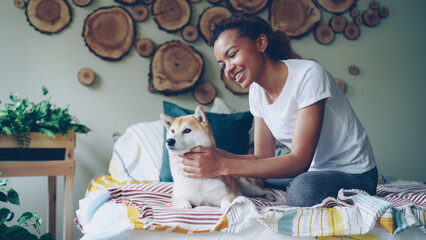 Happy African American teenage girl is caressing adorable pet dog stroking and kissing it...