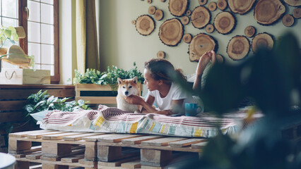 Caring dog owner is stroking adorable shiba inu dog and speaking to it lying on bed in modern apartment looking at animal with tenderness and love. People and pets concept.