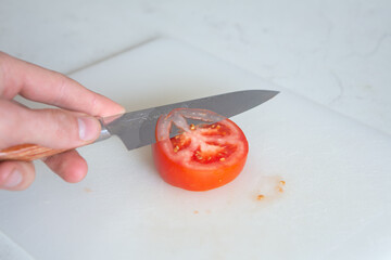 A sharp handcrafted Japanese Knife , slicing cleanly through a fresh tomato and other vegetables, skilled chef