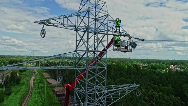 Parallex drone shot of technicians on lifting crane working on high voltage electricity tower in their uniform