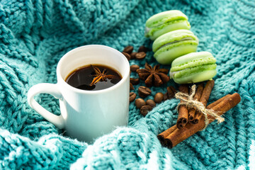 Obraz na płótnie Canvas A cup of coffee, a knitted turquoise sweater, an anise star, cinnamon sticks and macaroons. A cozy winter morning with a cup of coffee with cinnamon, star anise, a cozy sweater. Selective focus. 
