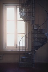 Vertical of sunshine lighting through a window beside a spiral staircase.