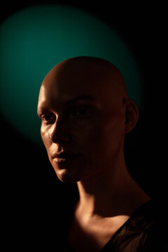 Portrait of bald young woman with blank expression against black background
