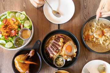 Assorted fusion food on wooden table. Wagyu beef with holy basil and chili fried rice,Roasted chicken with Japanese salad and fettuccine seared scallop with truffle cream sauce. Top view with someone.