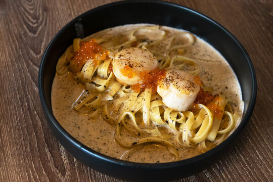 Fettuccine seared scallop with truffle cream sauce in black plate on wooden table background.