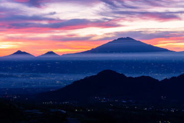 Fototapeta na wymiar A beautiful colorful epic reddish orange sunrise sky with mountain range and beautiful city lights - Magelang Regency looking out from slope of Mount Sumbing