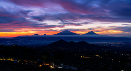 Beautiful colorful epic sunrise sky with mountain range and beautiful city lights, Magelang City and Merapi, Merbabu, Andong, Telomoyo mountain looking out from Sumbing Mountain - Mangli Village