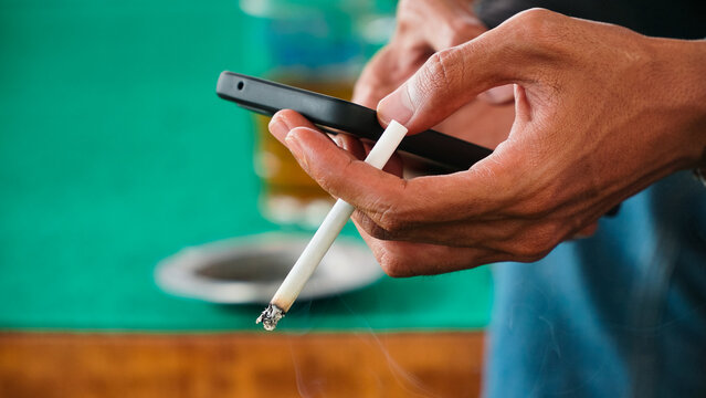 Magelang, Indonesia - October 23rd 2022 : Hand hold smartphone and cigarette