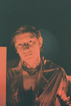 Portrait of young stylish man with tattoo looking at camera standing against black background