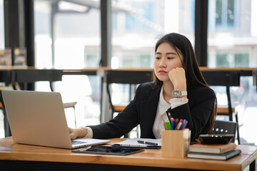 Asian businesswoman thinking, seriously and working with a laptop on the wooden table in the cafe.