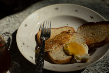 Bread and egg on plate. Breakfast on table. Details of ordinary food. Fork and plate in kitchen.