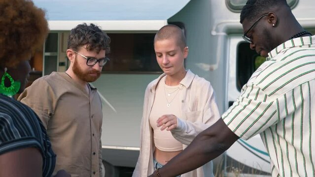 Four friends standing outside their white camper, joining hands, and throwing them up in the air saying hurray. Anti-racism concept. High quality 4k footage
