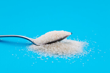 Steel spoon with sugar crystals on blue background