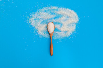 Wooden spoon with sugar crystals on blue background