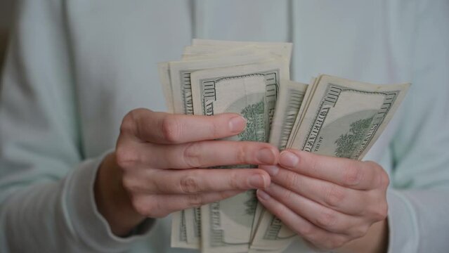 Women's hands hold American one hundred dollar bills, slowly counting them in absolute unwillingness to part with them in order to pay off the mortgage debt