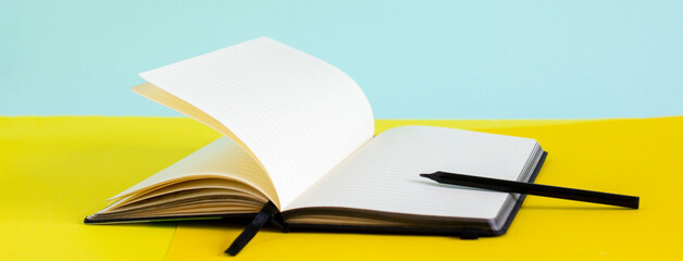 Open blank notebook and black pencil on yellow and blue background banner